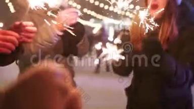 朋友们有乐趣的聚会与火花和自拍照片智能手机在圣诞节市场。 人们跳着舞